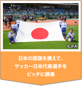 日本の国旗を携えて、サッカー日本代表選手をピッチに誘導